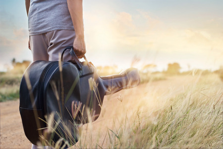 Guitar bag in hand on countryside road in nature backgroundの写真素材