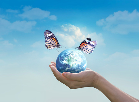 Woman holding planet earth with butterfly in hands on clean blue sky background, Elements of this image furnished by NASAの写真素材