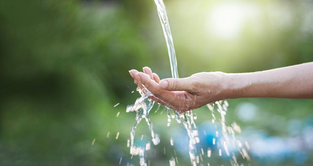 Water pouring in woman hand on nature background, environment issues