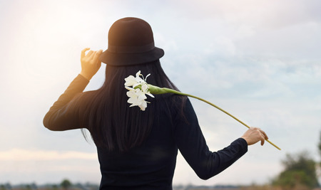 woman with white flower in hand relaxing outdoor in rural landscape sunset backgroundの写真素材