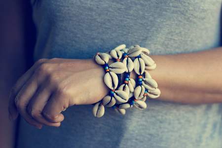 Cowrie shell bracelets on the wrist of woman, vintage color toneの写真素材