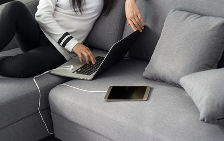 Woman using laptop and tablet sitting on the comfortable sofa at homeの写真素材