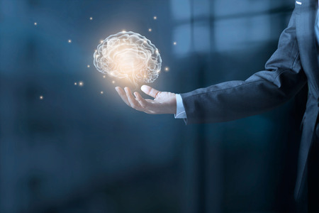 Businessman holding a brain and stardust in hand on blue office backgroundの写真素材
