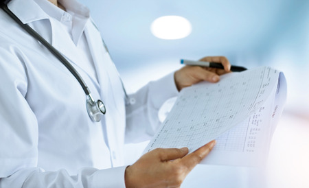 Woman doctor checking out and reading final reports in the room of a hospital backgroundの写真素材
