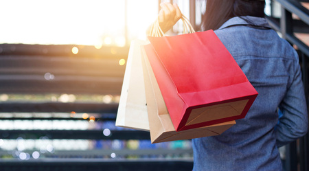 Rear view of woman holding shopping bag while up stairs outdoors on the mall backgroundの写真素材
