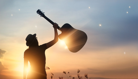 Musicien tenant la guitare dans la main sur fond de nature coucher de soleil