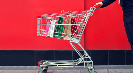 Woman shopper and shopping bag in a trolley or shopping cart on red wall the mall backgroundの写真素材