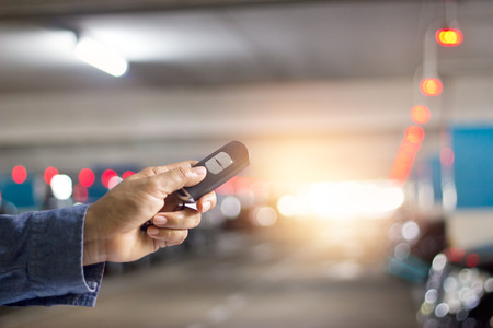Hand of holding and push key remote control of car on underground parking backgroundの写真素材