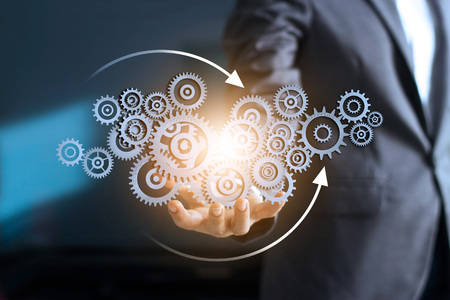 Business mechanism concept. Businessman holding with connected gears icons and business processes workflows on virtual screen.の写真素材
