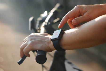 Woman cyclist hands with heart rate icon on smart watch, bicycle at summer trail. All on screen are design up.の写真素材