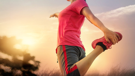 Young woman runner stretching legs before running at sunset rural trail.の写真素材