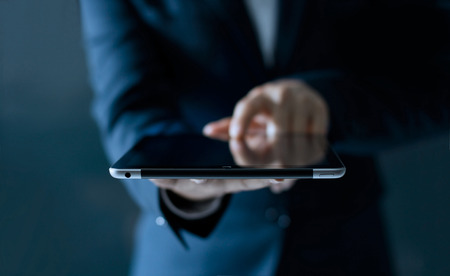 Businessman holding and touching digital tablet computer on dark background, business technology conceptの写真素材