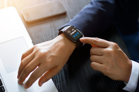 Businessman hands using smart watch app over laptop and smartphone on working desk, technology and communication concept. All on screen are design up.の写真素材