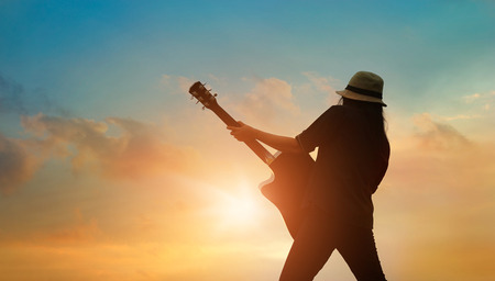 Guitarist playing acoustic guitar on the colorful cloudscape sunset backgroundの写真素材