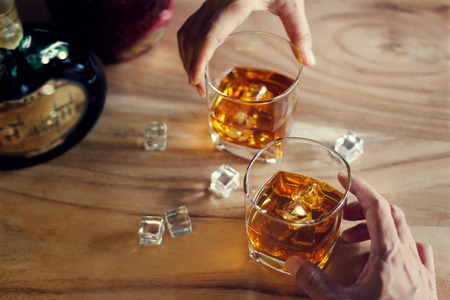 Close-up of two men clink glasses of whiskey drink alcoholic beverage together while at bar counter in the pubの写真素材