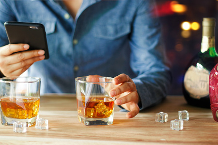 Man using smartphone while drink of whiskey alcoholic beverage at bar counter in the pubの写真素材
