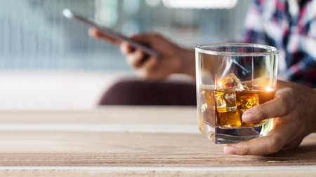 Man relaxing whith bourbon whiskey drink alcoholic beverage in hand and using mobile smartphone chat...