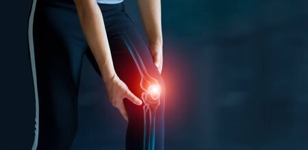Sport woman suffering from pain in knee. Tendon problems and Joint inflammation on dark background. Healthcare and medical.の写真素材