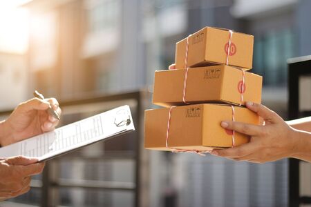 Delivery man holding parcel boxes while a man is signing documents in morning backgroundの写真素材