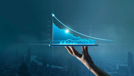 Businessman holding tablet and display graphs growth of business on virtual interface and stock market statistics gain profits on blue background.の写真素材