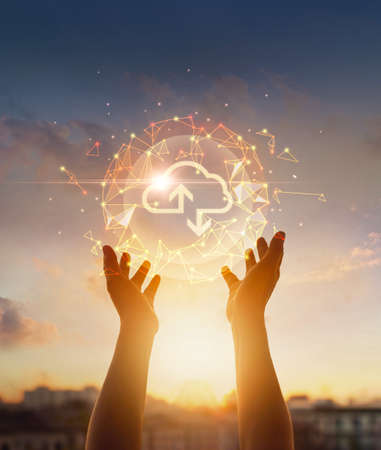 Cloud computing and networking concept. Hands touching global network and cloud icon on sunset background.の写真素材