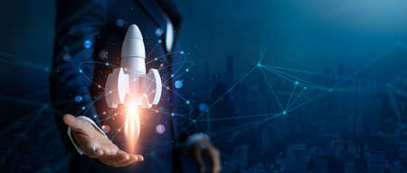 Startup business concept, Businessman control white rocket is launching and soar flying out from hand to sky for growth business,  Fast business success. Network connection on city background.の写真素材