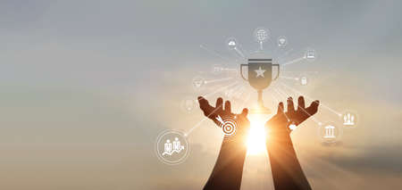 hands businessman touching a trophy of winner award and business icon of marketing on sunset background. business target. business goal success.の写真素材