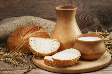Bread and bakery products, and milk in a clay jug and bowl, stalks of wheat, burlap on the old wooden backgroundの写真素材