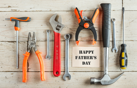 Greeting Card to Happy Father's Day, concept, set of different tools: a hammer, pliers, wrench, screwdriver, various spanners, clamp on a wooden background and tablet for an inscription,の写真素材