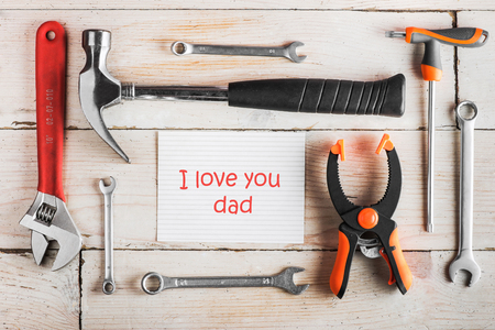 Greeting Card to Happy Father's Day,  Birthday Dad, concept, set of different tools: a hammer, wrench, screwdriver, various spanners, clamp on a wooden background and tablet with text I love you dadの写真素材