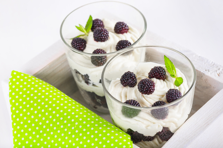 delicious soft cheese dessert with whipped cream and fresh blackberries with a sprig of fresh mint in a glass, in a decorative wooden box on a white tableの写真素材