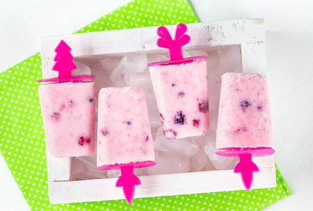 Homemade ice cream, frozen yogurt with blackberries, blueberries and raspberries, white wooden box with ice, bright green napkin in white polka dots print on a white table, top viewの写真素材