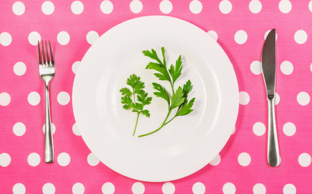 concept of healthy eating,  lose weight, vegetarian, vegan, raw food, potherb in the diet, sprig of fresh parsley, cilantro on a plate, fork and knife on a bright pink tablecloth with white polka dotsの写真素材