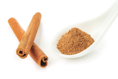 cinnamon powder in a white ceramic spoon and cinnamon sticks isolated on a white background closeupの写真素材