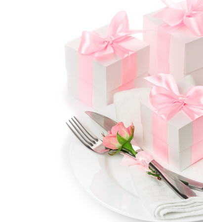 The concept of the holiday menu, knife, fork and a napkin on a plate with floral decoration, gifts with pink ribbon isolated on white backgroundの写真素材