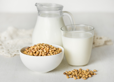 Soy milk in a glass and jar, soybeans on a white tableの写真素材