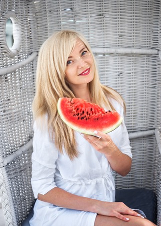 Young beautiful Caucasian blond woman smiling and holding a watermelon, summer conceptの写真素材