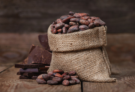 Raw unpeeled cacao beans and chocolate in the bag on the old wooden backgroundの写真素材