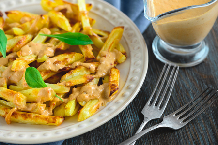 Baked potatoes with peanut sauce on a plate, napkin, fork and knife on a wooden table
