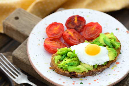 Fried tomatoes and avocado quail egg sandwich in a plate on a wooden background in a rustic styleの写真素材