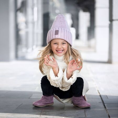 Cute little girl sitting and laughs in knitted hatの写真素材