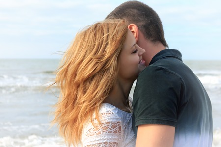 Blond and brunette teen couple hug together in beach outdoor at summer vacation. Sea waves on a background.の写真素材