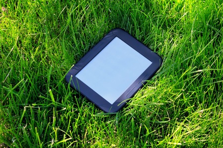 Black E-book reader lays on green grassの写真素材
