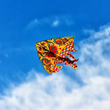Colorful bright kite flying in the wind on the blue sky backgroundの写真素材