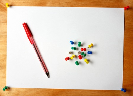 The standard A4 sheet of paper attached thumbtacks to a wooden board. On paper is a red pen and...
