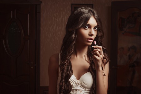 Beautiful young girl in negligee lipstick, looking in the mirror. Look at the camera.の写真素材