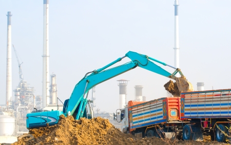 tractor excavator machine loading into dumper truck with industrial factory background