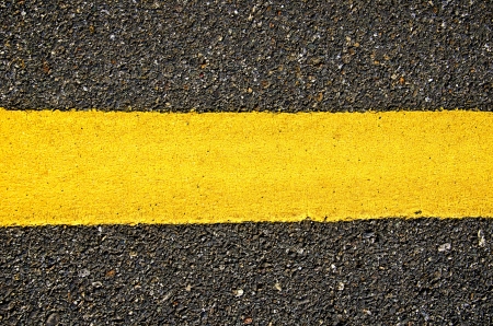 Texture closeup of an asphalt road with painted yellow line on the sideの写真素材