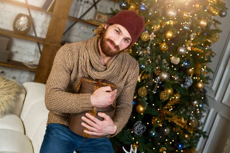 Man hugs his gift and thanked his girlfriend or wife for Christmas or new years surprise cozy apartments with Christmas tree hipster model in stylish sweaterの写真素材