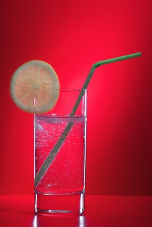A glass of lemonade and a straw on a red backgroundの写真素材